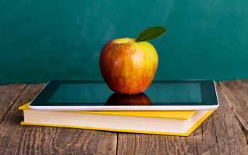 Omena, tabletti ja kirja opettajan pöydällä