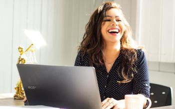 Nainen nauraa tietokoneen äärellä.