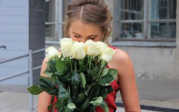 Juhla-asuinen tyttö nuuhkii ruusukimppua.