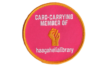 Pyöreä pinkki haalarimerkki, jossa keltainen nyrkki ja teksti Card-carrying member of haagahelialibrary.